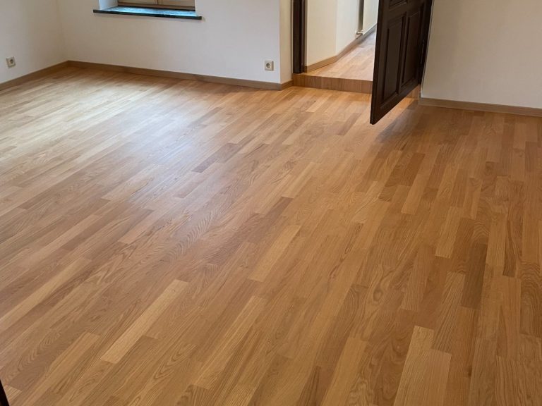 Stabparkettboden in einem leeren Raum mit geöffneten Türen, helle Wände.