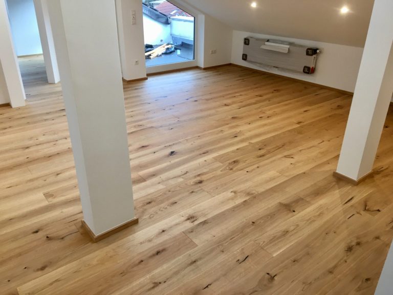 Holzfußboden in einem hellen Raum mit weißen Wänden und großen Fenstern.
