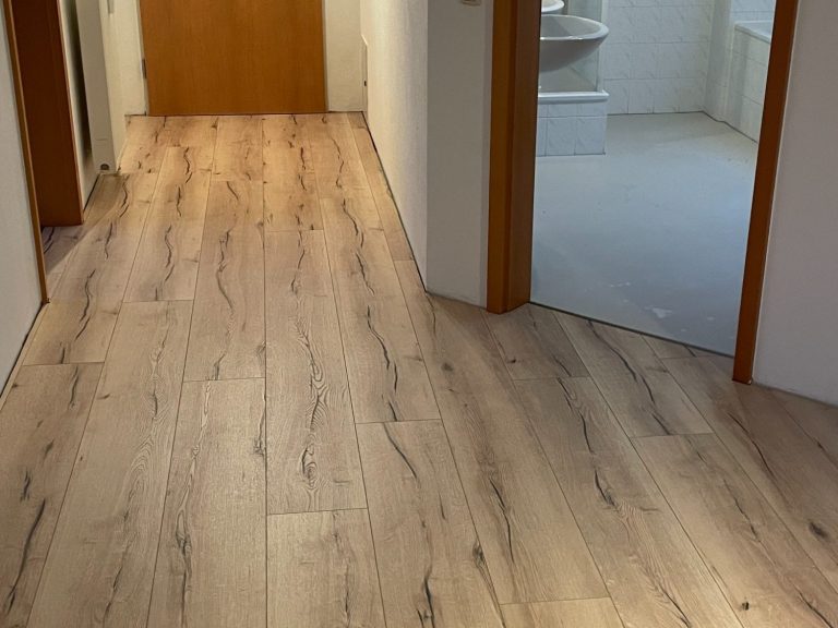 Langer Flur mit hellen Laminatböden und Zimmern auf beiden Seiten.