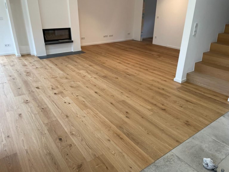 Helle Innenansicht mit Parkettboden und Treppe, Kamin an der Wand.