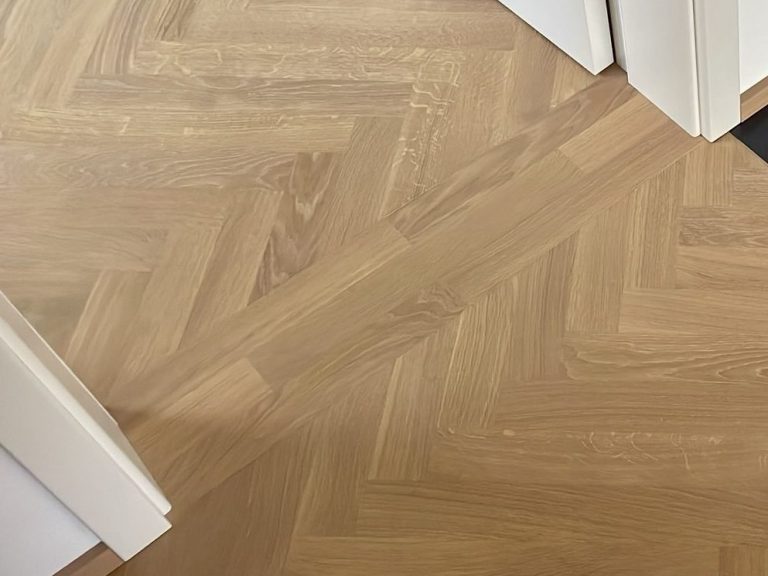 Holzboden im Fischgrätmuster mit warmen, hellen Tönen.