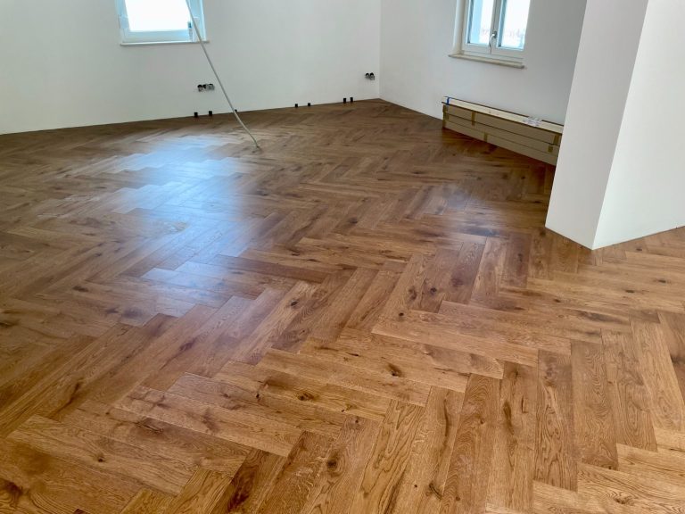 Parkettboden in Fischgrätmuster, leuchtend braun, in einem hellen Raum.