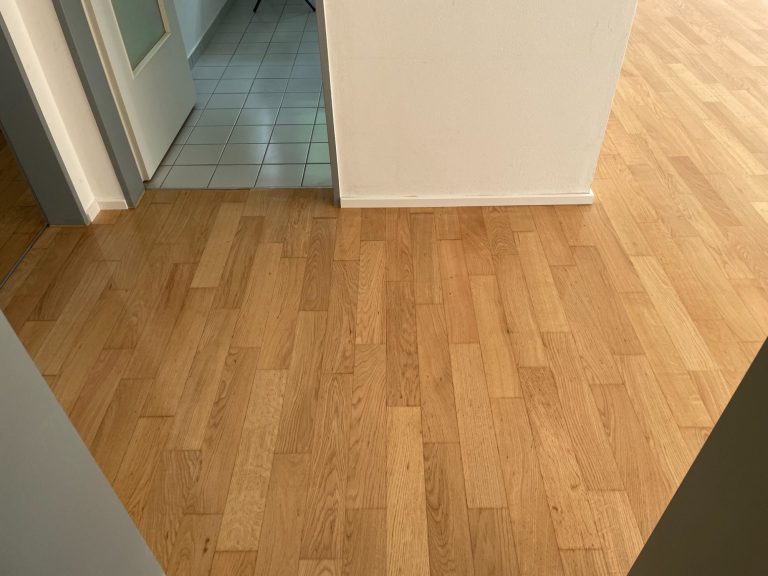 Parkettboden in einem Raum, helles Holz mit einem weißen Wandbereich im Hintergrund.