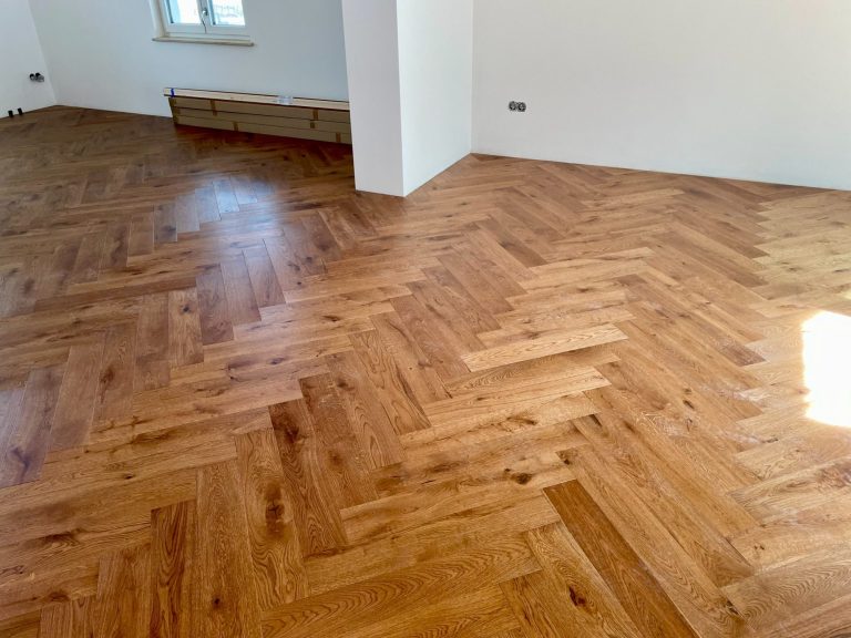Holzboden in Fischgrätmuster, hellbraun, in einem hellen Raum.