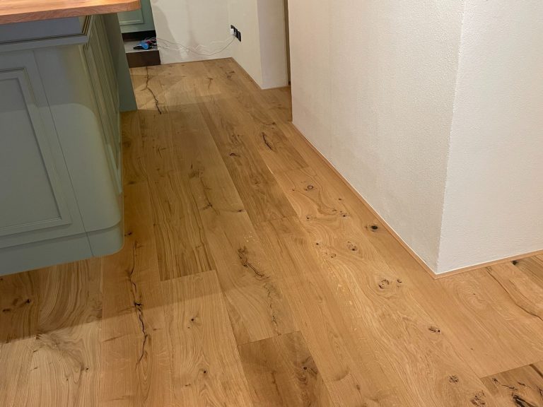 Breitdielenboden in warmen Farbtönen, mit Holzmaserung, an einer hellen Wand.
