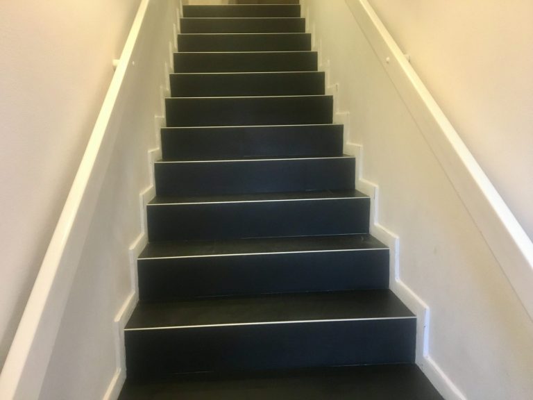 Eine gerade Treppe mit einem schwarz matten Klebevinyl in Fliesenoptik und weißen Wangen.